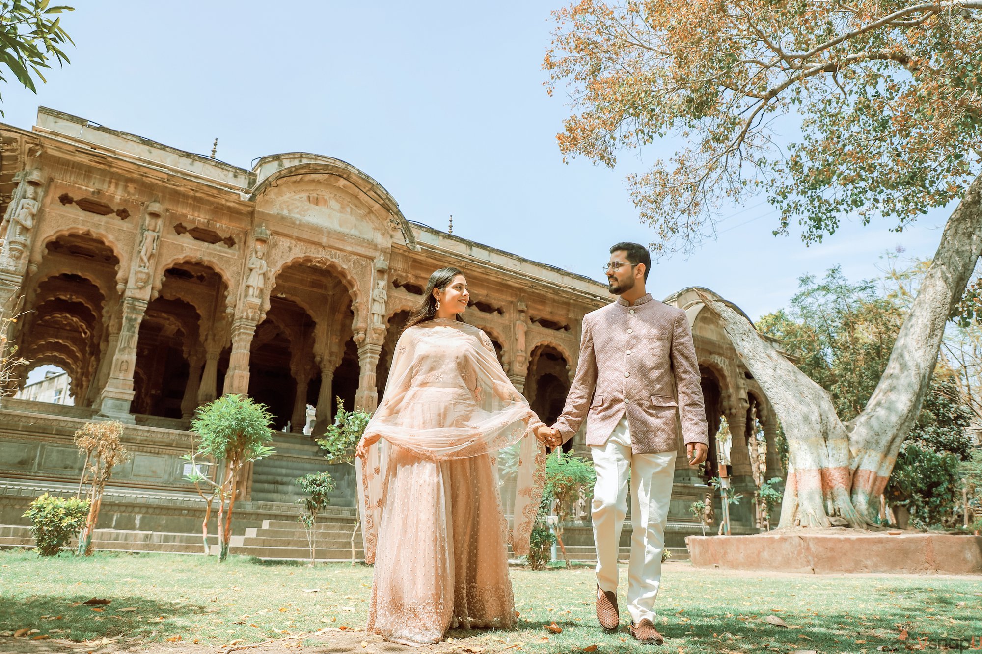 Traditional couple walking hand-in-hand in the lush garden of a fort, enjoying a peaceful and romantic pre-wedding moment.